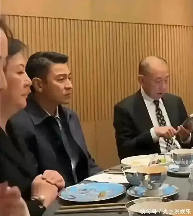64岁刘德华身穿西装在饭局上坐姿拘谨,双手搭在桌沿显僵硬